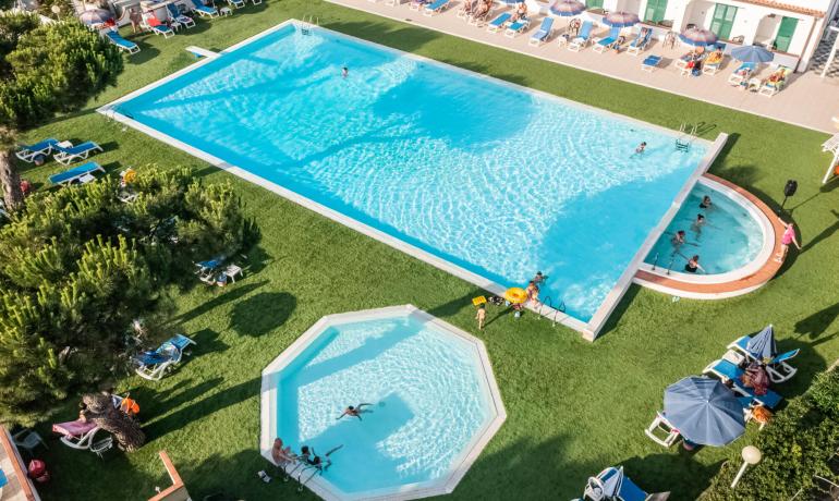 Piscina all'aperto con lettini e ombrelloni, persone che si rilassano.