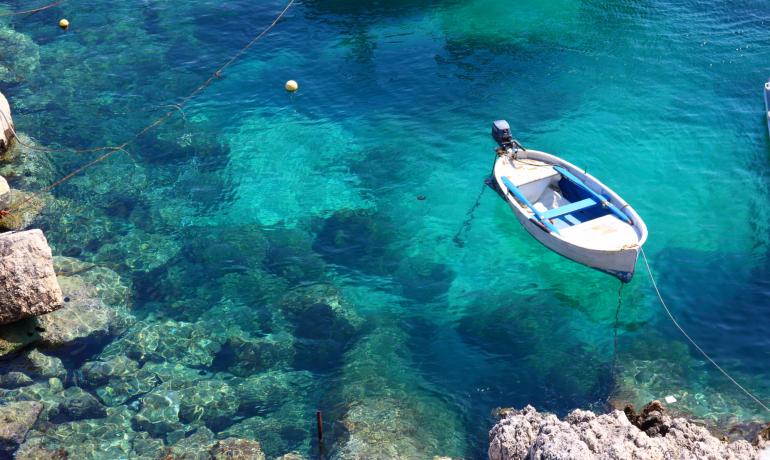 Barca bianca su acqua cristallina vicino alla costa rocciosa.