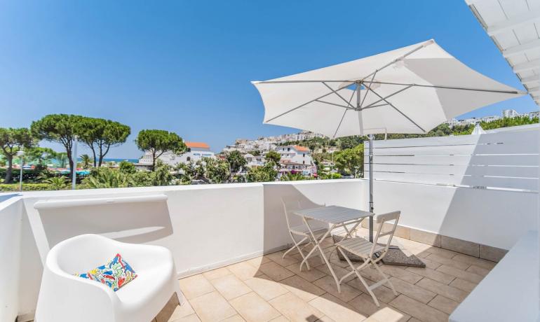 Terrazza con vista mare, arredi bianchi e ombrellone.