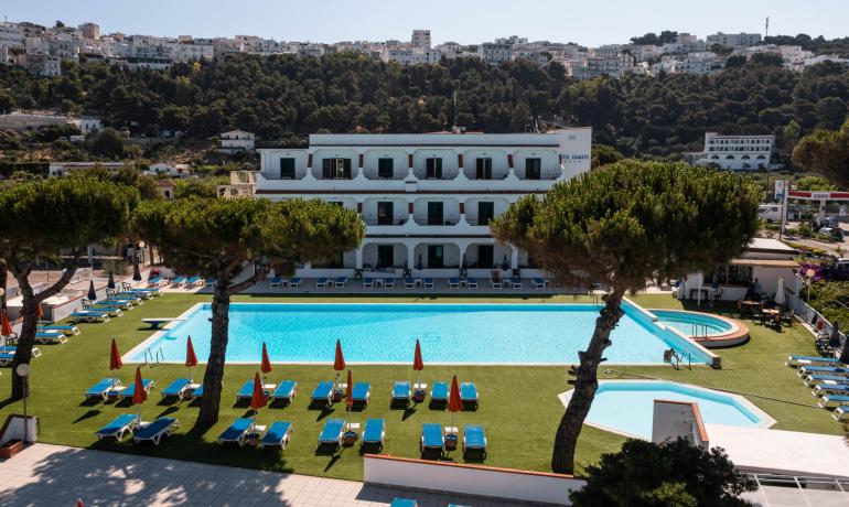 Hotel con piscina, circondato da colline e case bianche.