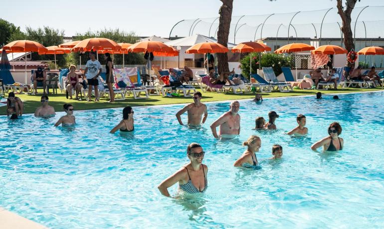 Persone si rilassano in piscina sotto ombrelloni arancioni.