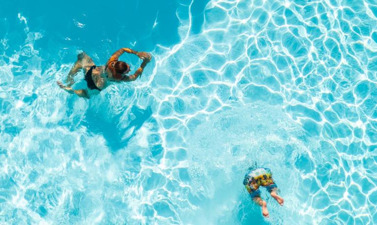 Due persone nuotano in piscina con acqua cristallina.